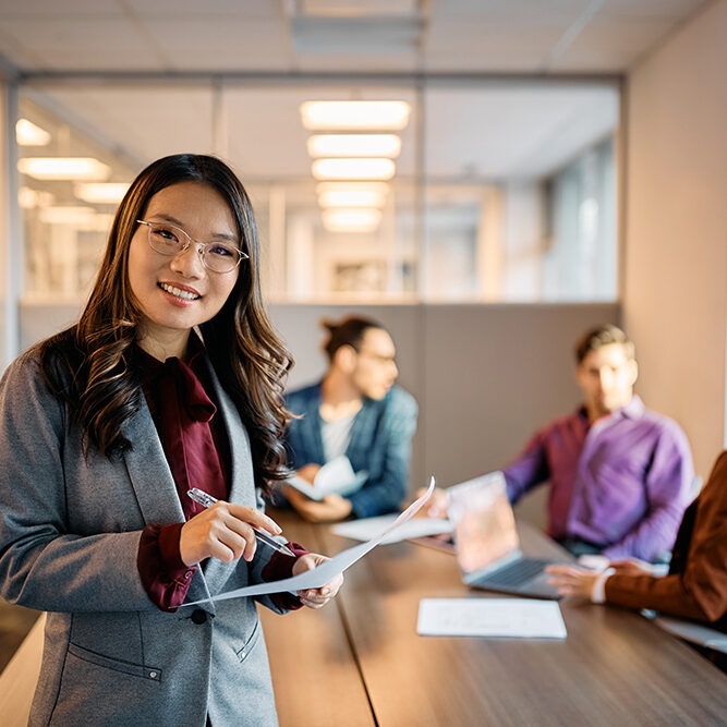 Happy Asian businesswoman working on reports during a meeting in the office and looking at camera.